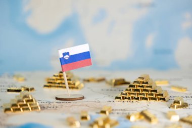 Ulusal ekonomik gücü, stratejik rezervleri ve finansal büyüme kavramını görselleştiren birçok küçük altın külçeyle çevrili bir dünya haritasına yerleştirilmiş minyatür bir Slovenya bayrağı