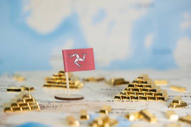 Haritada küçük bir Man Adası bayrağı ve parıldayan altın külçeleri açık deniz finansmanı, zenginlik yönetimi ve uluslararası finans stratejisini vurguluyor