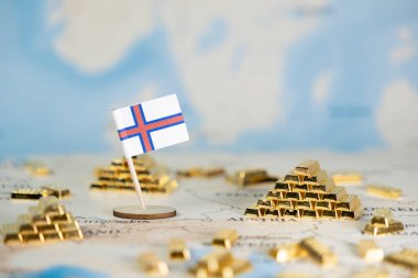Bir dünya haritasında Faroe Adaları bayrağı ve altın külçeleri ekonomik istikrar, küresel yatırım ve ulusal zenginlik planlamasını görselleştirir ve geniş bir kopya alanı sunar