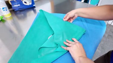 Eller titizlikle steril mavi ve yeşil perdeleri katlıyor, hastane hijyeni için tıbbi ekipman hazırlıyor ve güvenli klinik prosedürler uyguluyor.