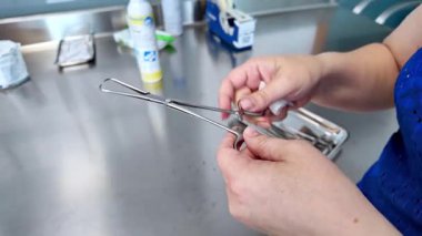 Temiz bir metal tezgahında cerrahi bir aleti dikkatlice manipüle ederek steril prosedüre hazır olduğunu vurgulayan bir sağlık uzmanının ellerine yakın plan.