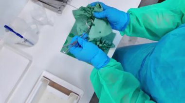 Korumadaki sağlık personeli titizlikle yeşil mendilli bir ameliyat aletini sterilize ederek hayati önem taşıyan hastane enfeksiyonunu kontrol ettiğini gösteriyor.
