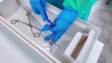 Bir sağlık çalışanının eldivenli elleri titizlikle sudaki metal tıbbi aletleri temizlerken, temel dezenfeksiyon ve sterilizasyon prosedürlerini vurguluyor.