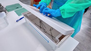 PPE 'deki sağlık uzmanının cerrahi aletlerle beyaz bir sterilizasyon tepsisi açması, temel temizlik ve steril tıbbi ekipmanların kullanımı konularında ayrıntılı görüşü