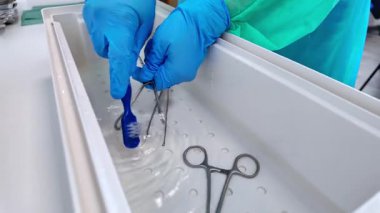 Sağlık çalışanı titizlikle tıbbi gereçleri suyla birlikte bir tepsiye koyuyor, titiz bir dezenfeksiyon ve güvenli tıbbi prosedürlere hazırlanmayı simgeliyor.