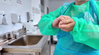 Tıbbi önlüklü ve plastik önlüklü bir kişinin yakın çekimi, elleri sıkıca bağlanmış, hijyen ve güvenlik protokolleri için gerekli kişisel koruma ekipmanlarını vurguluyor