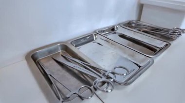 Ameliyat odası prosedürleri ve klinik operasyonları için gerekli olan steril metal tepsilerde bulunan parlak cerrahi aletlerin ve kıskaçların yakın çekimi.