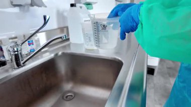 Eldivenli profesyonel, paslanmaz tezgahta bir laboratuvar bardağındaki temiz sıvıyı ölçer titiz bilimsel çalışmaları ve steril çevre protokollerini gösterir.