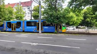 Poznan, Polonya - 1 Haziran 2025: Wroclaw ve Spotkajmy ile mavi tramvay, yeşil bir şehir parkında ilerliyor, kentsel toplu taşımayı temsil ediyor.