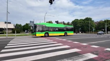 Poznan, Polonya - 1 Haziran 2025: Açık bir günde dinamik bir şehir kavşağından geçen parlak yeşil ve sarı bir elektrikli otobüs, çevre dostu toplu taşıma çözümlerini gösteriyor