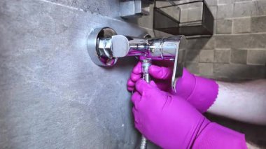 Pembe eldivenli eller krom banyo mikser musluğuna esnek bir metal duş hortumu yerleştiriyor, ev tesisatı kurulumunu ve tamir ihtiyaçlarını vurguluyor.