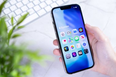 Poznan, Polonya - 10 Haziran 2025: Yeni iOS 26 arayüzü ve Sıvı Cam tasarımı içeren parlak bir akıllı telefonu tutan bir elin göz seviyesinde yakın plan çekimi