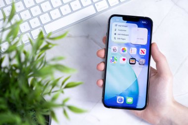 Poznan, Polonya - 10 Haziran 2025: Yeni iOS 26 arayüzünü masadaki Sıvı Glass tasarımı ve uygulama simgeleri ile gösteren akıllı telefon ekranı ile etkileşime giren kişinin eli