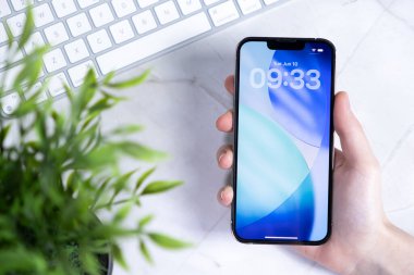 Poznan, Polonya - 10 Haziran 2025: Yeni iOS 26 arayüzünü canlı bir Sıvı Cam duvar kağıdıyla gösteren şık bir akıllı telefonu tutan bir elin üst görüntüsü
