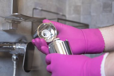 Yakın plan bir perspektif, parlak pembe eldivenlerle bir duş suyu filtresini dikkatlice sökerek, daha iyi arındırma için gerekli DIY ev bakımını gösterir.