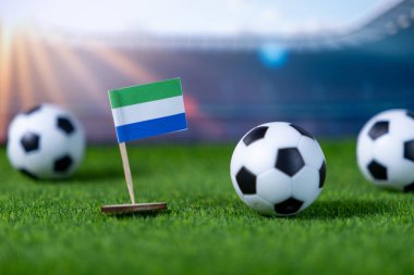 Sierra Leone bayraklarına yakın çekim. Yapay sahada duran minyatür futbol topları spor için vatansever desteğini gösteriyor.