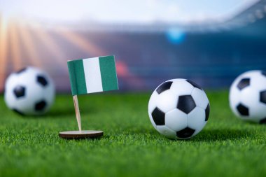 Nijerya bayrağının, yemyeşil bir çim tarlasına yerleştirilmiş futbol toplarının yanına yakın plan, ulusal gurur ve atletizm yarışmasını sembolize ediyor.