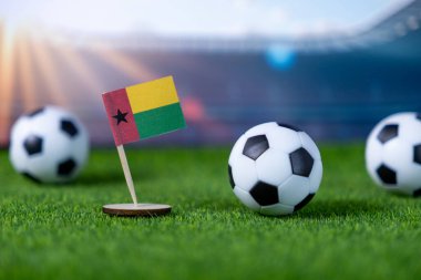 Gine-Bissau 'nun ulusal bayrağına ve yapay yeşil çimlere yerleştirilmiş çoklu minyatür futbol toplarına odaklanın.