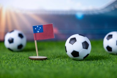 Close-up of a small Samoa national flag and miniature soccer balls on artificial green grass, symbolizing global sporting events and national team participation