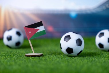 Futbol toplarıyla yeşil çimlerin üzerinde minyatür Jordan bayrağı, ulusal spor başarılarını ve futbol müsabakaları için vatansever birliği simgeliyor