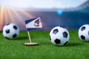Ulusal gurur, atletik rekabet ve küresel spor müsabakalarını sembolize eden, canlı yeşil bir alana yerleştirilmiş futbol toplarıyla küçük Amerikan Samoa bayrağı.