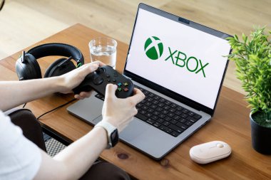 Poznan, Polonya - 15 Haziran 2025: Bilgisayarında Xbox logosu olan bir kişi modern etkileşimli dijital oyun deneyimini gösteren bir denetleyici tutuyor