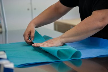 Yetenekli ellerin yakından çekimi mavi tıbbi kumaşı dikkatlice katlayarak, klinik ortamda kritik tıbbi malzemeler için sterilite ve organizasyonu sağlar.