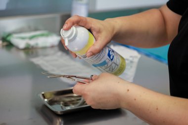 Titiz eller metal cerrahi aletlere antiseptik sprey sıkarak sterilizasyon ve tıbbi güvenlik için gerekli hijyen uygulamalarını vurguluyor.