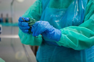 Bir sağlık uzmanının koruyucu üniformalı eldivenli elleri titizlikle tıbbi bir aleti temizler, gerekli hijyen protokollerini ve hasta güvenliğini ön plana çıkarır.