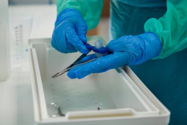 Bir sağlık uzmanının eldivenli elleriyle steril bir kaptaki fırçayla cerrahi aletleri temizlerken, hastanın güvenliği için tıbbi hijyen ve dezenfekte sürecini vurguluyor.