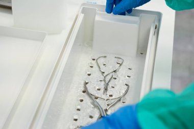 Tıbbi bir tepside dezenfektan sıvısına batırılmış cerrahi aletlerin yakın görüntüsü klinikteki enfeksiyon kontrolü için titiz bir temizlik olduğunu gösteriyor.