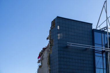 Kısmen yıkılan bir şehir binasının detaylı görüntüsü, yıkılan beton ve tuğla ile parlak, modern, karanlık bir cephe arasındaki zıtlığı vurguluyor.