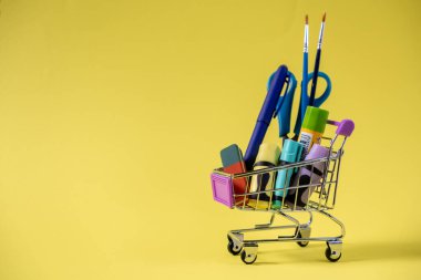 Okula dönüş, eğitim ve perakende kavramları için kalem, makas ve fosforlu minyatür alışveriş arabası.