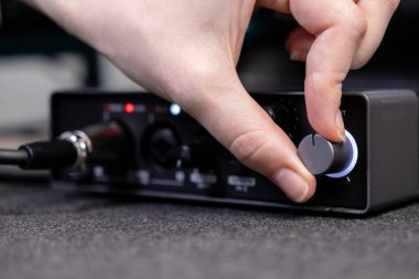 Stüdyoda kayıt, podcast ve dijital içerik üretimi için hassas ses kontrolünü gösteren parlak siyah bir ses kartının kadranını çeviren elin yakın çekimi