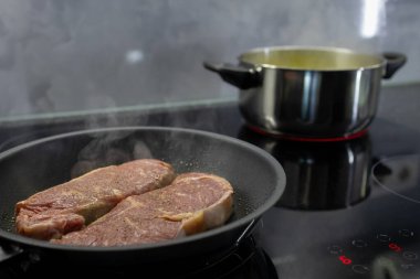 Modern bir indüksiyon kabında buharlı iki çiğ biftek, yemek pişirme, akşam yemeği hazırlama ve sağlıklı bir yaşam tarzını ön plana çıkarıyor.