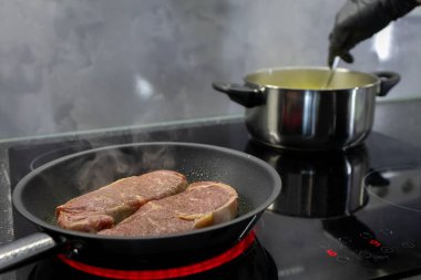 Işıl ışıl yanan kırmızı bir tencerede kızaran iki baharatlı çiğ bifteğin yakın çekimi, modern mutfak verimliliğini ve gurme yemek yaratımını vurguluyor