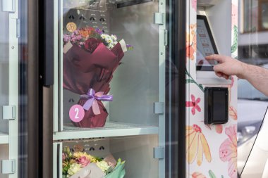 Bir elin yakın çekimi, modern perakende kolaylığı ve anlık hediyeleri gösteren, self-servis çiçek büfesinden canlı taze bir buket seçiyor.