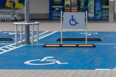Üzerinde uluslararası tekerlekli sandalye sembolü olan geniş mavi bir park alanı ve bir perakende mağazasının yanında gerekli erişilebilir park yeri sağlayan bir tabela.