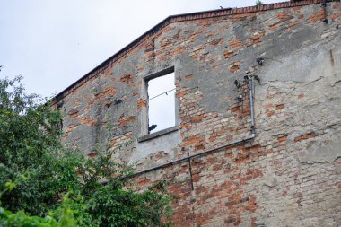 Çürüyen bir tuğla binanın ön cephesi boş bir pencere çerçevesi ve beton soyarken, unutulmuş bir geçmiş, yıkım ve kentsel dönüşümü akla getiriyor.