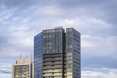 Poznan, Polonya - 13 Temmuz 2025: ATANER binası, yansıtıcı pencerelerle çağdaş gökdelenlere çarpıyor, bulutlu gökyüzü altında kentsel gökyüzüne hükmediyor, modern kurumsal mimari sergiliyor