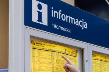 Poznan, Polonya - 13 Temmuz 2025: Bir istasyon bilgi panosundaki Odjazdy Gidiş sarı takvimine işaret eden kişi, yolculara yardım ediyor