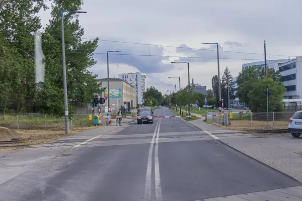 Poznan, Polonya - 13 Temmuz 2025: Demiryolu geçidinde engelleri aşmış bir araba bekliyor, bisikletli insanlar yakınlarda trafik güvenliğini gösteriyor