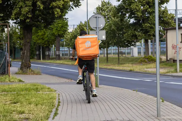 Swarzedz, Polonya - 13 Temmuz 2025: Pyszne.pl bisikletli kurye şehir kaldırımında büyük turuncu yalıtılmış teslimat çantasıyla, kentsel yemek siparişlerini yerine getiriyor