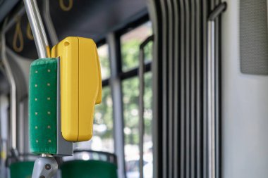 Modern bir şehir otobüsünün içinde parlak sarı stop düğmesi ve yeşil kumaş destek direğine yakın plan, verimli toplu taşıma, kentsel taşıma ve yolcu deneyimini vurguluyor