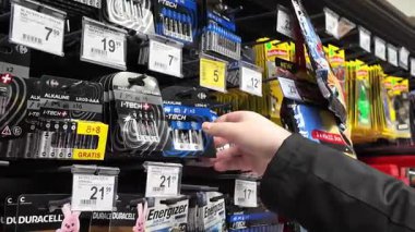 Poznan, Polonya - 28 Mayıs 2025: Parlak ışıklandırılmış bir süpermarket rafındaki ev pillerini inceleyen bir müşterinin yakın çekimi, günlük tüketici tercihlerini ve kullanılabilir ürünleri yansıtıyor