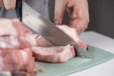 Becerikli bir elin keskin bir bıçakla çiğ domuz etini dilimlediği yakın plan görüntüsü, gıda güvenliği, taze malzemeler ve mutfak hazırlıkları.