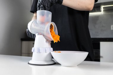 Siyah eldivenli bir insanın elle öğütülmüş turuncu havuçlarıyla besleyici ev yemekleri için beyaz bir kaseye düşüşünü yakından çek.