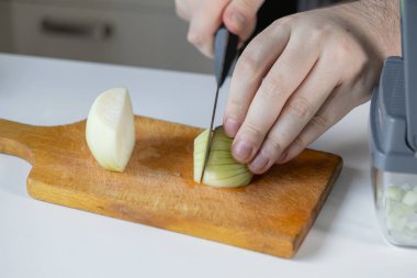 Ahşap bir tahtanın üzerinde taze beyaz soğan doğramak için bıçak kullanan insan elinin yakın plan görüntüsü, ev yemekleri ve sağlıklı yemek hazırlama sürecini gösteriyor.
