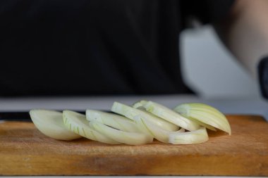 Üniformalı beyaz soğan dilimlerinin yakını, ahşap bir tahtanın üzerinde, gurme ya da günlük yemek pişirme için hazırlanan ham maddeleri gösteriyor.