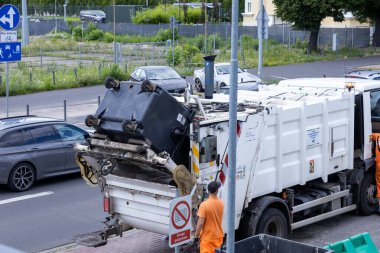 Poznan, Polonya - 29 Temmuz 2025: Çöp konteynırını kaldıran büyük bir kamyonu, temizlik için kentsel atıkları toplayan bir işçiyi gösteren bir sokak manzarası